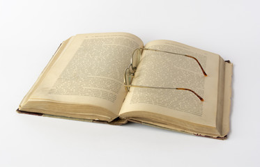 Old book and reading glasses on white background