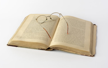 Old book and reading glasses on white background