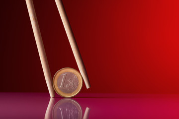 One euro coin and chopstick over red background