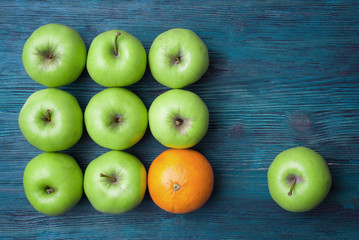 Green apples and one orange on blue wooden background