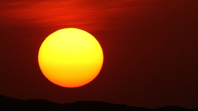 huge sun setting behind desert dunes