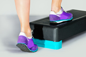 Female feet in violet sneakers on fitness step.