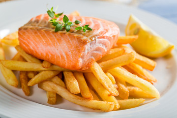 Tasty french fries with salmon served on plate with lemon