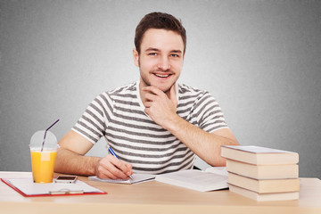 Young man sitting at the table with a pile of books