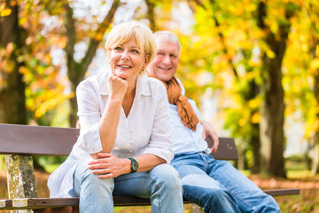 Älteres Paar sitzt auf Park Bank im Herbst - obrazy, fototapety, plakaty