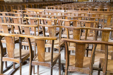 Rows of many worn wooden chairs in a church