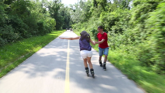 Happy young couple rollerblading on a wonderful sunny day in park, holding hands