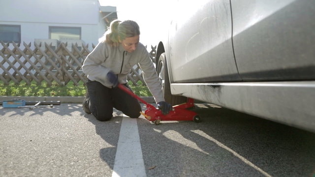woman lifting car with jack to change tires
