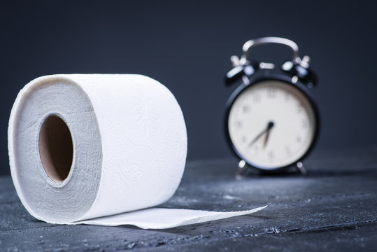 Alarm clock with toilet paper on a black wooden table