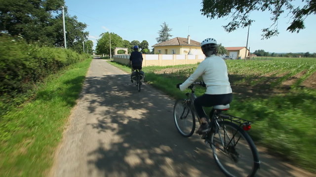 Slow motion - Retired couple cycling on road in village in France