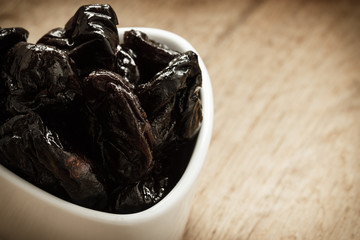 dried plums prunes in white bowl on wooden table