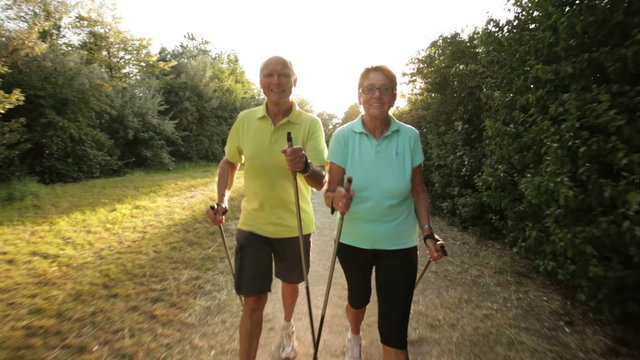tracking shot happy smiling retirees nordic walking in late afternoon
