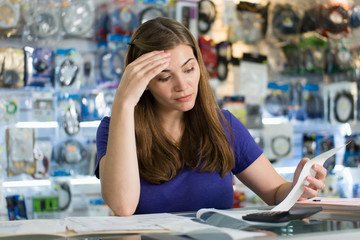 Worried Woman Checking Bills And Invoices In Computer Shop