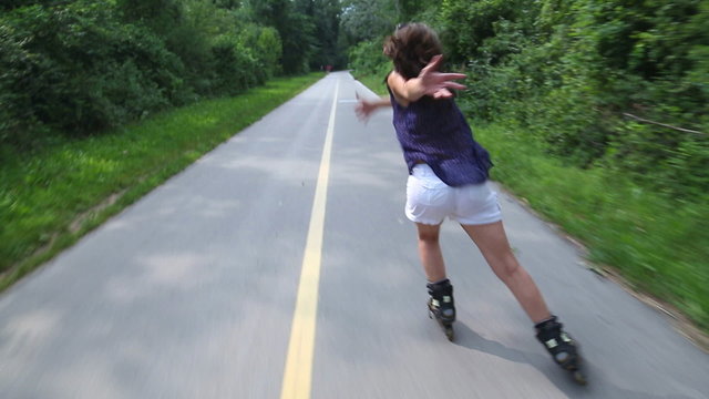 Young attractive woman rollerblading in park on a beautiful sunny day from back
