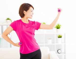 Naklejka premium happy young woman exercising with dumbbells in living room