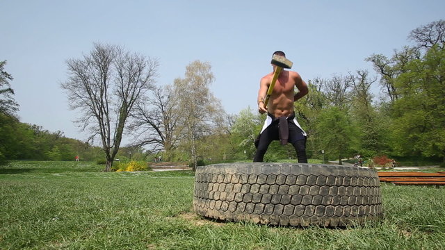 Muscular man hitting tire with a hammer with only one hand