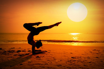 Fototapeta na wymiar Silhouette young woman practicing yoga on the beach at sunrise