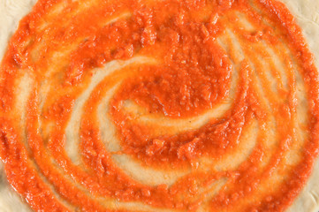 close up of adding tomato sauce to pizza base