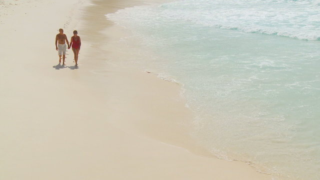 Active Senior Couple Walking Towards Camera Along Beach With Waves
