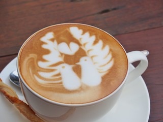 Latte art coffee and biscuit stick on the wooden desk.