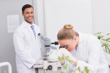 Happy scientist smiling at camera using microscope