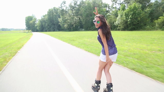 Young attractive woman rollerblading in park on a beautiful sunny day from back with hands in the air