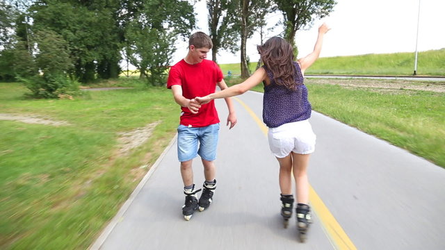 Young woman and man rollerblading and performing in park on a beautiful warm day, holding hands.