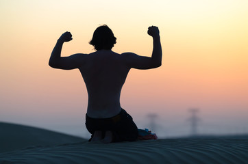 The man silhouette at sunset in desert sitting on his knees