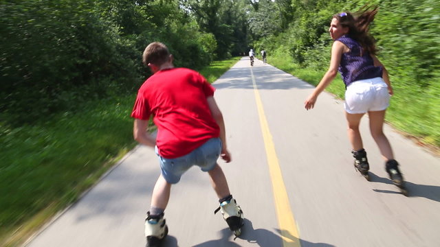 Young woman and man rollerblading on a beautiful sunny summer day in park, holding hands
