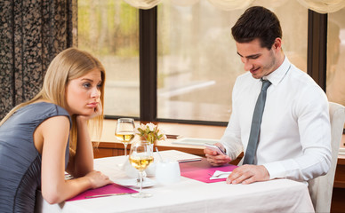 Woman is bored at restaurant, her boyfriend is typing sms