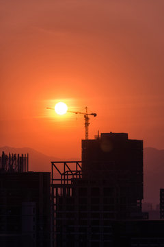 Industrial construction cranes and building silhouettes over sun