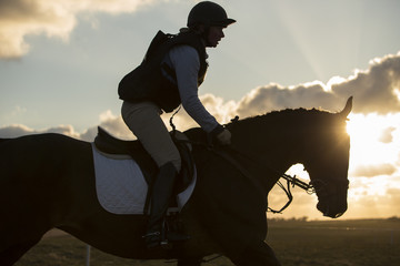 Horse and rider galloping in evening light. Backlit.