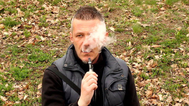 man vaping e cigarette outdoor in the field