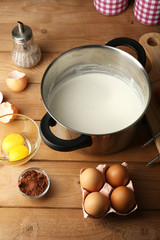Preparation cream with eggs in pan on wooden background