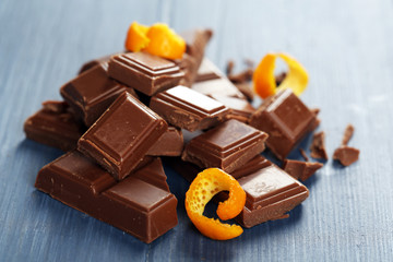 Pieces of chocolate with orange peels on wooden background