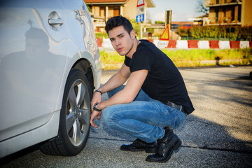 Handsome Man Sitting Besides the Wheel of Car Changing Tires