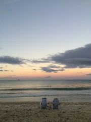 A couple enjoys the sunset from two beach chairs