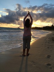 A woman does a sun salutation at sunrise on Kailua Beach Oahu