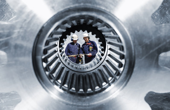 industry workers seen through a giaant gear shaft