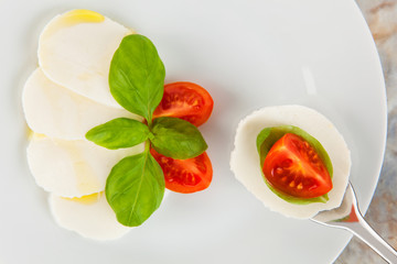 Mozzarellasalat mit Tomaten und Basilikum auf einer Gabel