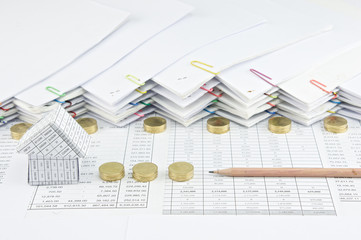 House with brown pencil between pile of gold coins