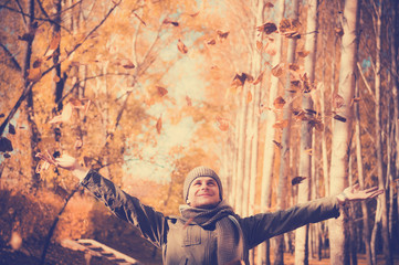 Young man having fun throwing up piles of autumn leaves .