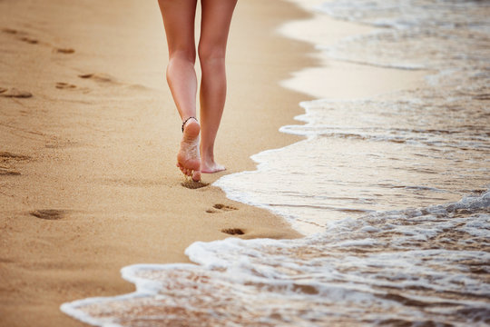Beautiful young woman is walking along a seashore leaving footpr