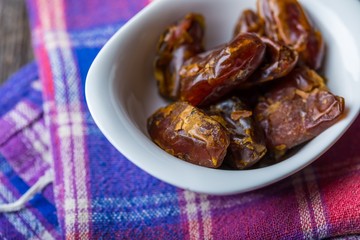 Dried dates in bowl on wooden table..