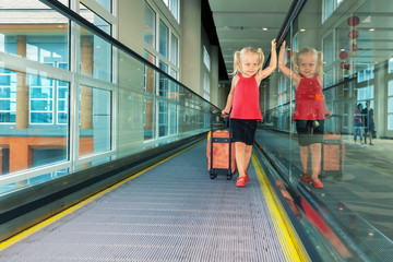 Joyful girl with her trunk on airport moving walkway