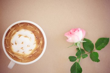 A cup of coffee with latte art and pink rose on brown paper back