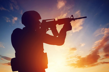 Soldier shooting with his rifle at sunset. War, army, military.