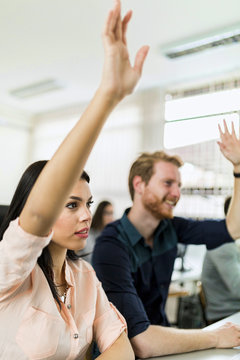 Beautiful Young Woman And A Man Raising Hands In Classroom