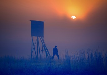 Naklejka premium Man standing near raised hide at sunrise