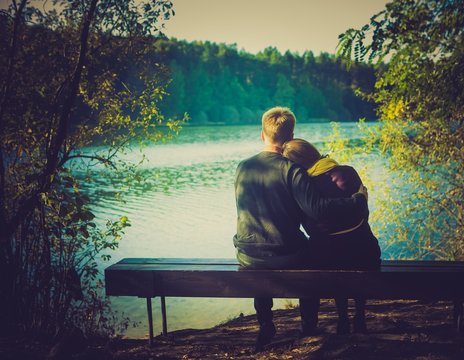 Silhouettes of hugging couple sitting on bench 